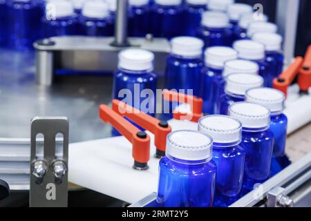 Blaue Kunststoffflasche auf der Produktionslinie des Förderbandes an der Abfüllmaschine in der medizinischen Fabrik. Pharmazeutische Fertigung. Stockfoto