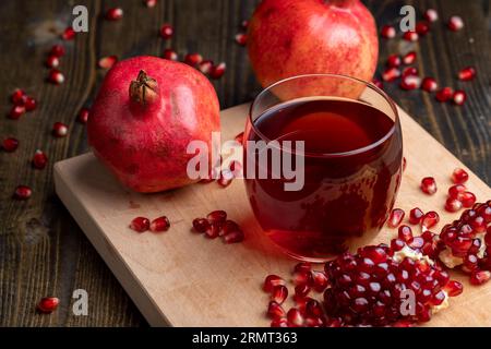 Süßer und saurer Granatapfelsaft in einem transparenten Glas auf dem Tisch, daneben rote reife Granatäpfel mit großen süßen Körnern Stockfoto