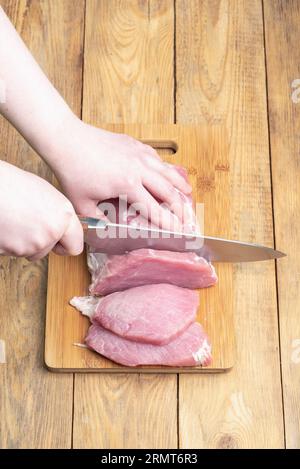 Eine Frau schneidet rohes Fleisch auf einem Schneidebrett in Stücke. Leerzeichen kopieren. Stockfoto