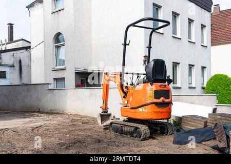 Kleiner oranger Raupenbagger auf einer Baustelle in der Nähe eines Wohngebäudes. Stockfoto