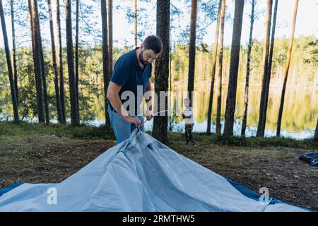 Der süße kaukasische Junge hilft dem Vater, ein Zelt aufzubauen. Familiencampingkonzept Stockfoto