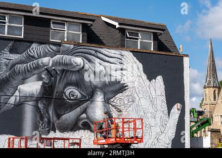 Southend on Sea, Essex, Großbritannien. 30. August 2023. Southend, das als Europas größtes Street-Art-Festival bezeichnet wird, feiert mit dem City Jam-Event seinen neuen Stadtstatus weiter. Über 200 lokale, nationale und internationale Straßenkünstler zeigen ihre Fähigkeiten an 100 Orten im Stadtzentrum. Einige provisorische Mauern wurden errichtet, aber die Künstler schmücken auch die Seiten von Gebäuden und andere dauerhafte Strukturen. Vom ersten bis zum dritten September haben die Künstler mit der Arbeit an den größeren Wandgemälden begonnen, um für die Veranstaltung bereit zu sein. Männlicher Künstler, der an grossen Fototapeten arbeitet Stockfoto