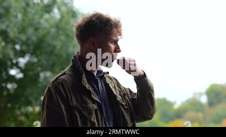 Nahaufnahme. Seitenansicht des jungen, gutaussehenden Mannes, der draußen einen Vape raucht. Lässige, nachdenkliche, männliche, rauchende elektronische Zigarette im Freien Stockfoto