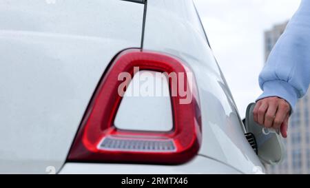 Die Nahaufnahme der weiblichen Hände öffnet den Ladeanschluss des Fahrzeugs und führt das Ladekabel in das Elektroauto. Die Fahrerin lädt das Elektrofahrzeug beim Laden auf Stockfoto