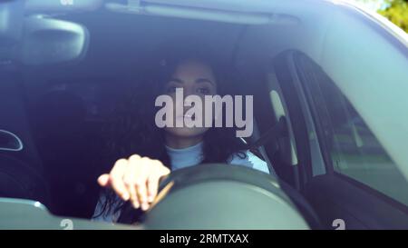 Attraktive positive lächelnde brünette Frau im Auto, die ein drehendes Lenkrad fährt und auf die Straße schaut. Kaukasische junge Geschäftsfrau fährt Auto Stockfoto