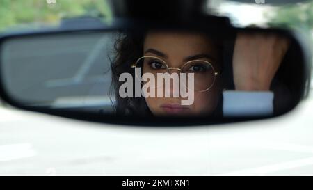 Nahaufnahme einer jungen Frau, die beim Autofahren auf den Rückspiegel schaut und ihr Haar berührt. Reisekonzept. 4K-Video. Wunderschönes Weibchen Stockfoto