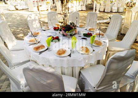 Elegante Banketttische, die für eine Konferenz oder eine Party vorbereitet sind und mit einer weißen Tischdecke bedeckt und mit Blumen für Gäste dekoriert sind Stockfoto