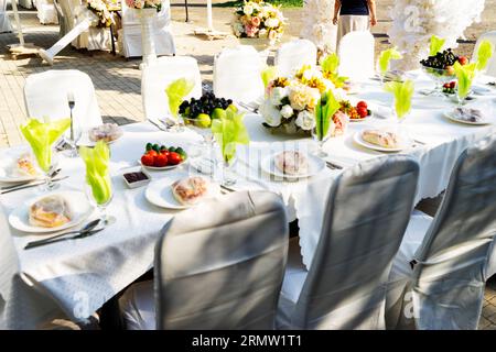 Elegante Banketttische, die für eine Konferenz oder eine Party vorbereitet sind und mit einer weißen Tischdecke bedeckt und mit Blumen für Gäste dekoriert sind Stockfoto