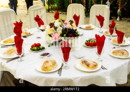 Elegante Banketttische, die für eine Konferenz oder eine Party vorbereitet sind und mit einer weißen Tischdecke bedeckt und mit Blumen für Gäste dekoriert sind Stockfoto
