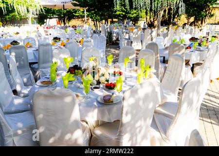 Elegante Banketttische, die für eine Konferenz oder eine Party vorbereitet sind und mit einer weißen Tischdecke bedeckt und mit Blumen für Gäste dekoriert sind Stockfoto