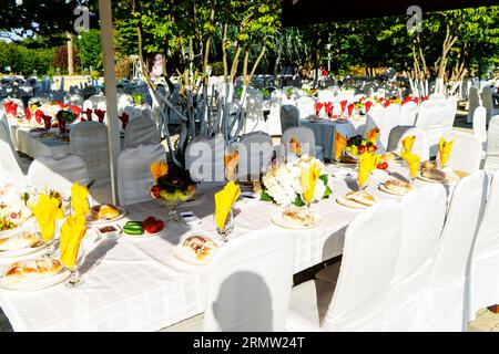 Elegante Banketttische, die für eine Konferenz oder eine Party vorbereitet sind und mit einer weißen Tischdecke bedeckt und mit Blumen für Gäste dekoriert sind Stockfoto