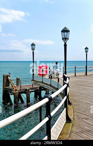 Eine einsame weibliche Figur, die am Ende des Worthing Pier an einem klaren Sommertag in Worthing West Sussex England auf das Meer blickt Stockfoto