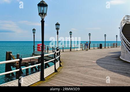 Eine einsame weibliche Figur, die am Ende des Worthing Pier an einem klaren Sommertag in Worthing West Sussex England auf das Meer blickt Stockfoto