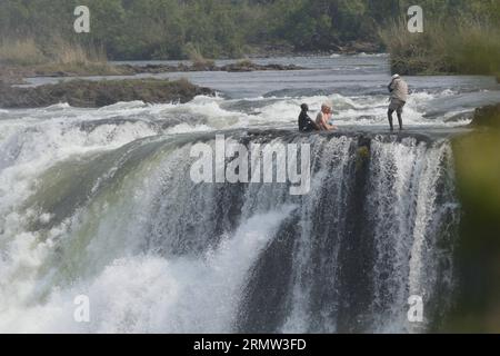 (141002) -- VICTORIA FALLS, -- ausländische Touristen posieren für Fotos mit lokalen Reiseleitern am Teufelspool auf den Victoria Falls, an der Grenze von Simbabwe und Sambia, 30. September 2014. Das Teufelsbecken ist während der Trockenzeit ein wichtiger Ort für Touristen an den Victoria Falls, besonders in den Monaten September und Oktober, wenn die Wasserstände am niedrigsten sind und die Strömung des Zambezi River mild ist. Das Schwimmen im Pool, der sich am Rande der 108 Meter hohen Victoria Falls befindet, wird nur von ortskundigen Reiseleitern geschützt und gilt als einer der aufregendsten Touris Stockfoto