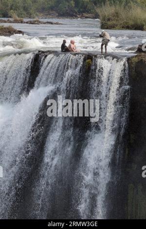 (141002) -- VICTORIA FALLS, -- ausländische Touristen posieren für Fotos mit lokalen Reiseleitern am Teufelspool auf den Victoria Falls, an der Grenze von Simbabwe und Sambia, 30. September 2014. Das Teufelsbecken ist während der Trockenzeit ein wichtiger Ort für Touristen an den Victoria Falls, besonders in den Monaten September und Oktober, wenn die Wasserstände am niedrigsten sind und die Strömung des Zambezi River mild ist. Das Schwimmen im Pool, der sich am Rande der 108 Meter hohen Victoria Falls befindet, wird nur von ortskundigen Reiseleitern geschützt und gilt als einer der aufregendsten Touris Stockfoto