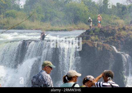 (141002) -- VICTORIA FALLS, -- ausländische Touristen posieren für Fotos mit lokalen Reiseleitern am Teufelspool auf den Victoria Falls, an der Grenze von Simbabwe und Sambia, 30. September 2014. Das Teufelsbecken ist während der Trockenzeit ein wichtiger Ort für Touristen an den Victoria Falls, besonders in den Monaten September und Oktober, wenn die Wasserstände am niedrigsten sind und die Strömung des Zambezi River mild ist. Das Schwimmen im Pool, der sich am Rande der 108 Meter hohen Victoria Falls befindet, wird nur von ortskundigen Reiseleitern geschützt und gilt als einer der aufregendsten Touris Stockfoto