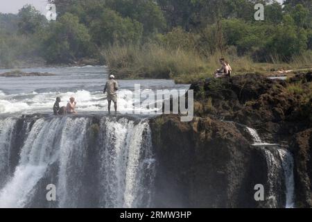 (141002) -- VICTORIA FALLS, -- ausländische Touristen posieren für Fotos mit lokalen Reiseleitern am Teufelspool auf den Victoria Falls, an der Grenze von Simbabwe und Sambia, 30. September 2014. Das Teufelsbecken ist während der Trockenzeit ein wichtiger Ort für Touristen an den Victoria Falls, besonders in den Monaten September und Oktober, wenn die Wasserstände am niedrigsten sind und die Strömung des Zambezi River mild ist. Das Schwimmen im Pool, der sich am Rande der 108 Meter hohen Victoria Falls befindet, wird nur von ortskundigen Reiseleitern geschützt und gilt als einer der aufregendsten Touris Stockfoto
