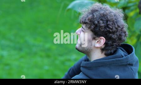 Seitenansicht Sportler entspannt sich, massiert sein Bein, spürt Schmerzen im Bein. Mann sitzt im grünen Park auf einer Betonbank. Aktivitäten im Freien. Stockfoto