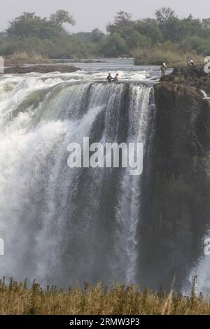 (141002) -- VICTORIA FALLS, -- ausländische Touristen posieren für Fotos mit lokalen Reiseleitern am Teufelspool auf den Victoria Falls, an der Grenze von Simbabwe und Sambia, 30. September 2014. Das Teufelsbecken ist während der Trockenzeit ein wichtiger Ort für Touristen an den Victoria Falls, besonders in den Monaten September und Oktober, wenn die Wasserstände am niedrigsten sind und die Strömung des Zambezi River mild ist. Das Schwimmen im Pool, der sich am Rande der 108 Meter hohen Victoria Falls befindet, wird nur von ortskundigen Reiseleitern geschützt und gilt als einer der aufregendsten Touris Stockfoto