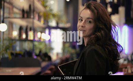 Kaukasische Frau, die als Gastgeberin im Restaurant arbeitet, läuft durch das Café und zeigt den Ort und spricht mit der Kamera. Stockfoto