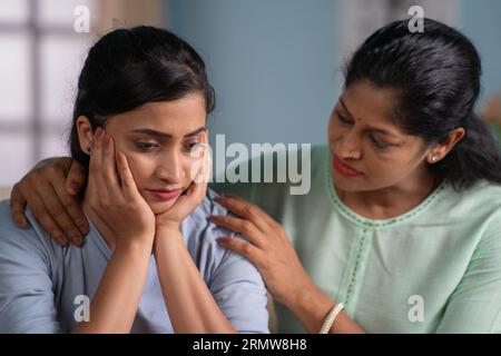 Indische Mutter tröstet ihre traurige oder besorgte erwachsene Tochter zu Hause - Konzept von Familienunterstützung, Mutterschaft und bedingungsloser Liebe Stockfoto