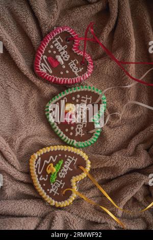 3 Lebkuchen mit farbenfroher Creme und Band liegen auf braunem Stoffhintergrund aus nächster Nähe von oben. Weihnachtsessen Stockfoto