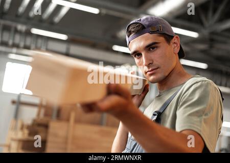 Junger Zimmermann sucht und wählt Holzbohle in einer Werkstatt in einer Holzfabrik Stockfoto