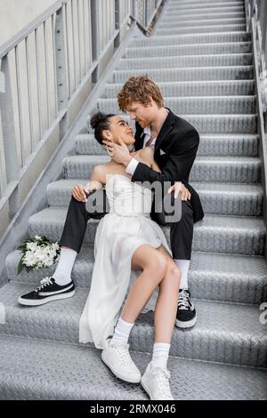 Urbane Romantik, Liebe, Hochzeit im Freien, junges, interrassisches Paar, das sich in der Nähe von Blumen auf Treppen umgibt Stockfoto