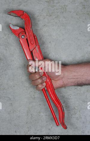 Roter Rohrschlüssel in der Handwerkerhand. Konzentrierte Handwerkskunst, perfekte Ausführung, Qualität und Zuverlässigkeit. Stockfoto