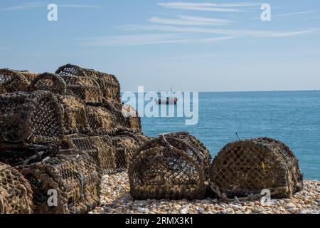 Hummerfallen am Strand mit einem Fischerboot im Meer im Hintergrund in Selsey West Sussex England Stockfoto