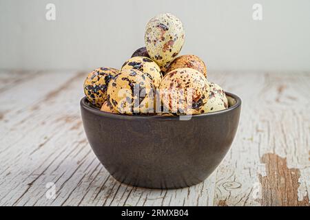 Eine weiße, unberührte Oberfläche mit einer Keramikschale gefüllt mit kleinen, gesprenkelten Wachteleiern, die darauf ruhen Stockfoto