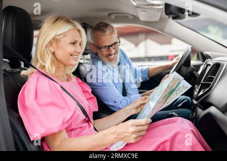 Lächelnde ältere Freunde, die mit dem Auto zusammen reisen, überprüfen die Karte Stockfoto