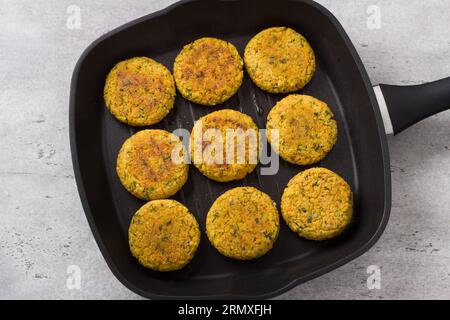 Vegane Hirsenschnitzel mit Karotten, Grünzeug und Samen in einer Pfanne auf grauem strukturiertem Hintergrund, Draufsicht. Hausgemachtes veganes Essen. Stockfoto