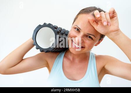 Kopfschuss einer sportlich lächelnden Frau, die Schaumstoffrolle auf der Schulter hält und lächelt Stockfoto