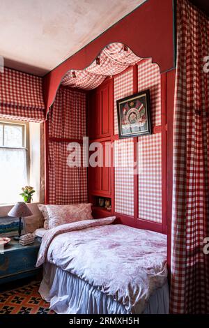 Roter Gingham-Stoff umgibt ein Einzelbett in einem aus dem 18. Jahrhundert stammenden Blumenloft in der Nähe von Penzance in Cornwall, Großbritannien Stockfoto
