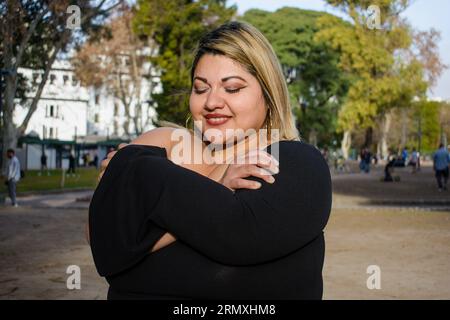 Junge, große argentinische Latina-Frau, die im Park steht und sich umarmt und sich selbst liebt, lächelt glücklich bei Sonnenuntergang. People Concept, Copy Space. Stockfoto