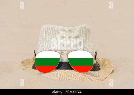 Sonnenbrillen mit Gläsern in Form einer bulgarischen Flagge und einem Hut liegen auf Sand. Konzept der Sommerferien und Reisen in Bulgarien. Sommerruhe Stockfoto