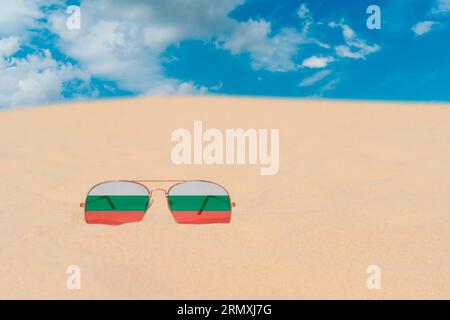 Sonnenbrillen mit Gläsern in Form einer bulgarischen Flagge liegen auf Sand gegen blauen Himmel. Konzept der Sommerferien, Reisen und Tourismus in Bulgarien Stockfoto