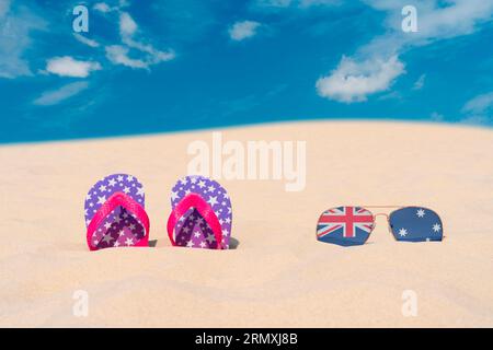 Sonnenbrillen mit Brille in Form einer australischen Flagge und Flip-Flops liegen auf Sand am blauen Himmel. Konzept von Sommerferien und Reisen in Australien Stockfoto