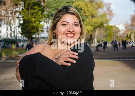 Junge, große argentinische Latina-Frau, die im Park steht und sich umarmt und sich selbst liebt, lächelt glücklich bei Sonnenuntergang. People Concept, Copy Space. Stockfoto