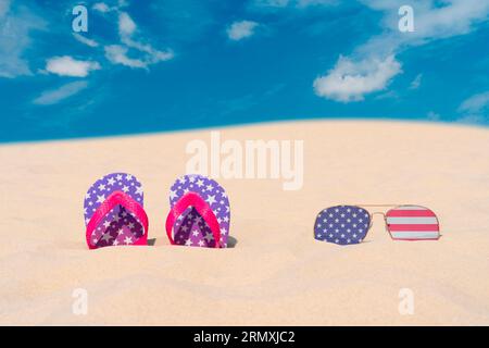 Sonnenbrillen mit Brillen in Form der Flagge der USA und Flip-Flops liegen auf Sand gegen blauen Himmel. Konzept von Sommerferien und Reisen in den USA Stockfoto