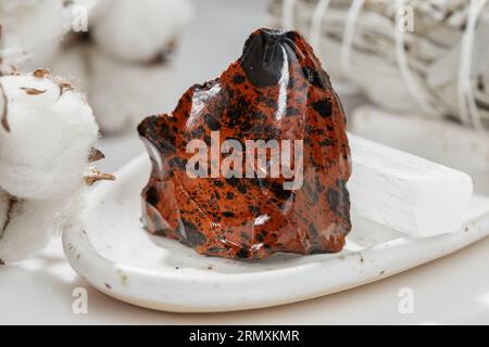 Ungeschnittenes Mahagoni-Obsidian- oder Vulkanglas-Mineral-Stein-Exemplar auf dem Keramiktablett über hellem Hintergrund Stockfoto