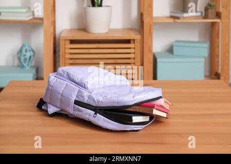 Stilvoller Schulrucksack mit Büchern auf Holztisch im Wohnzimmer Stockfoto