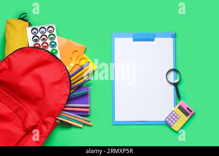 Stylischer Schulrucksack und verschiedene Schreibwaren auf grünem Hintergrund Stockfoto