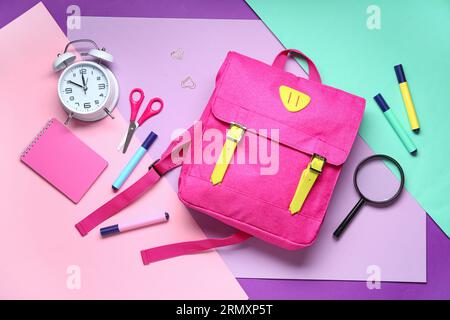 Stylischer Schulrucksack mit verschiedenen Schreibwaren auf farbigem Hintergrund Stockfoto