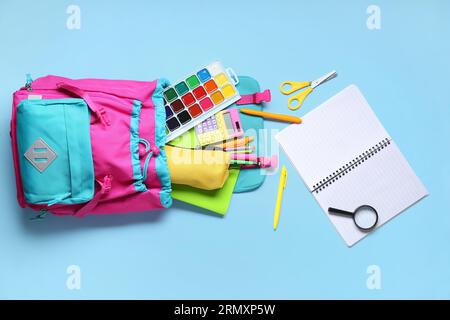 Stylischer Schulrucksack mit verschiedenen Schreibwaren auf blauem Hintergrund Stockfoto