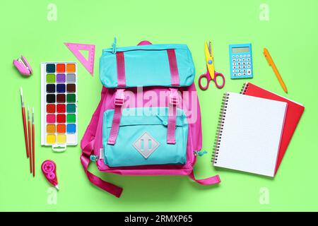 Stylischer Schulrucksack und verschiedene Schreibwaren auf grünem Hintergrund Stockfoto
