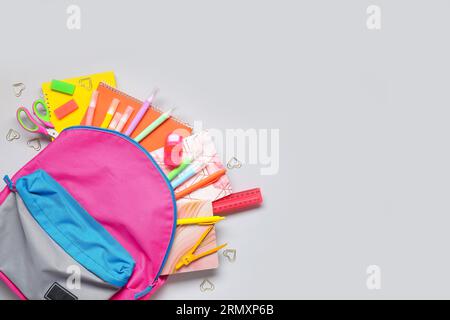 Stylischer Schulrucksack mit verschiedenen Schreibwaren auf grauem Hintergrund Stockfoto