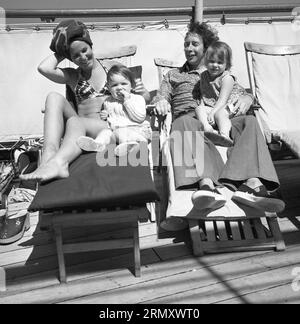 1960er Jahre, historisch, Kreuzfahrt, eine Familie, die sich mit ihren zwei kleinen Kindern auf Liegestühlen auf dem Deck eines Kreuzfahrtschiffs entspannt. Stockfoto