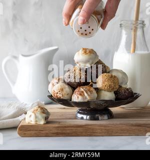 Eine Hand, die Zimt auf einen Haufen Kürbis-Gewürztrüffel streut. Stockfoto
